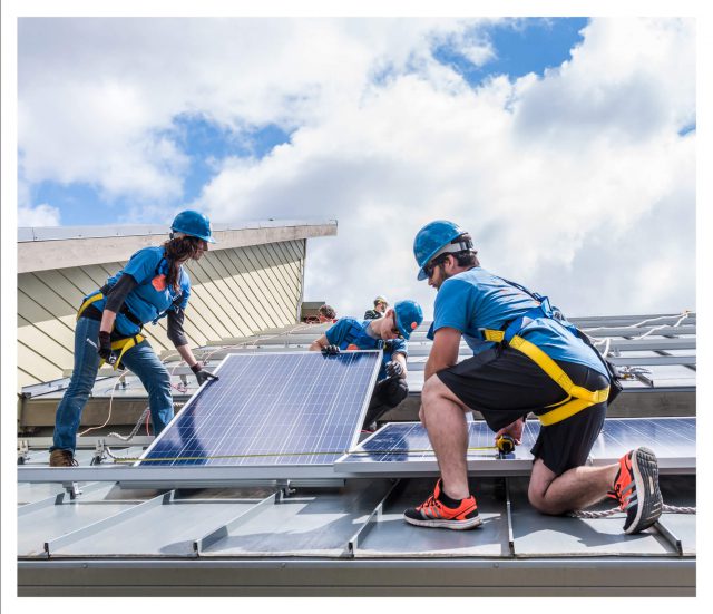 A photo of three workers installing solar panels on a roof.